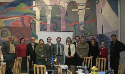 Fotografie de grup a participanților la întâlnire, în sala de ședințe, cu drapelele României și ale Uniunii Europene pe masă