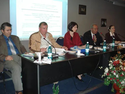 Prezidiu de cinci persoane la masa de conferință, în fața ecranului de proiecție, la al doilea workshop, noiembrie 2007